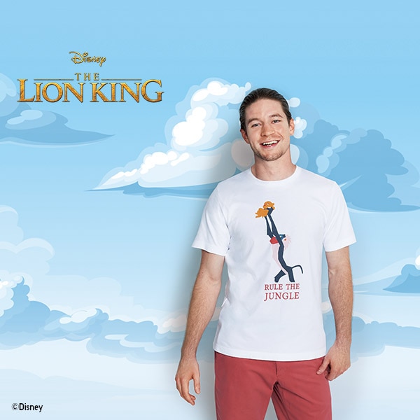 A man wears a white The Lion King Collection T-shirt featuring a print of Raifiki holding Simba aloft