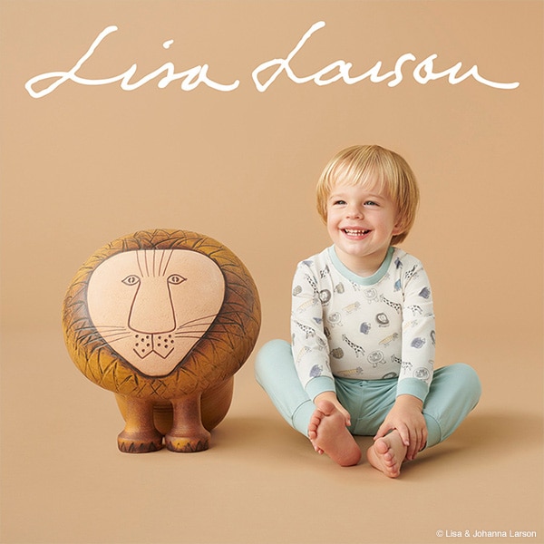 A young boy in white and blue Lisa Larson UT pyjamas smiles next to one of Larson's popular lion sculptures.