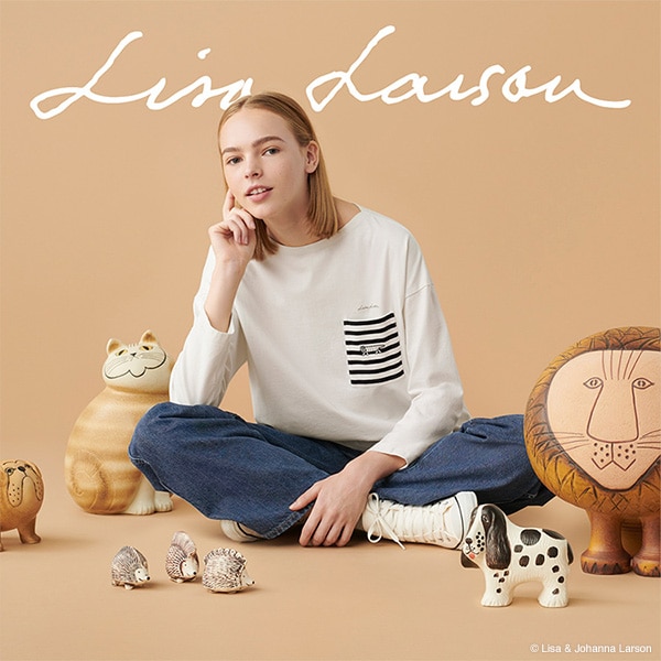 Une femme porte le T-shirt blanc de la collection UT Lisa Larson, assise parmi des sculptures d’animaux par l’artiste.