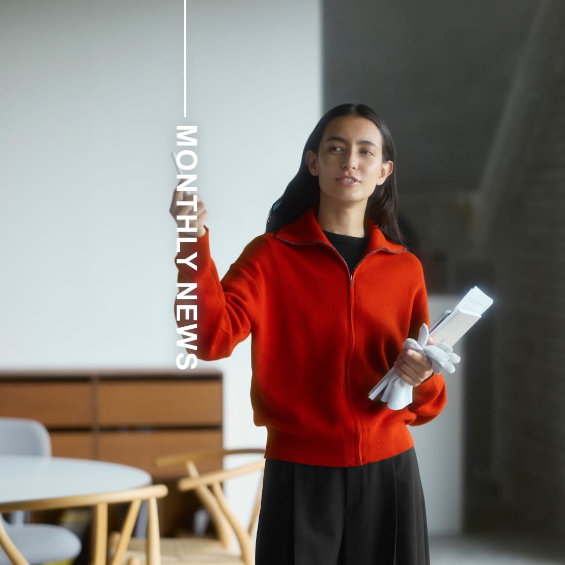model wearing zip-up cardigan in red over a black crew neck with black trousers while giving a presentation next to the words monthly news