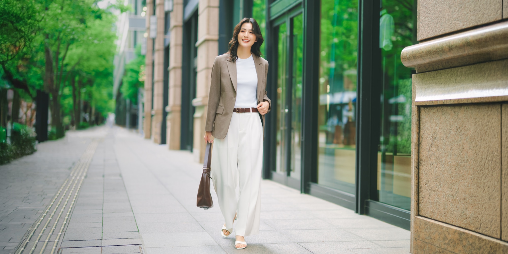 model wearing smart pleated wide trousers in off white with a white T-shirt and light brown blazer and a brown belt and bag