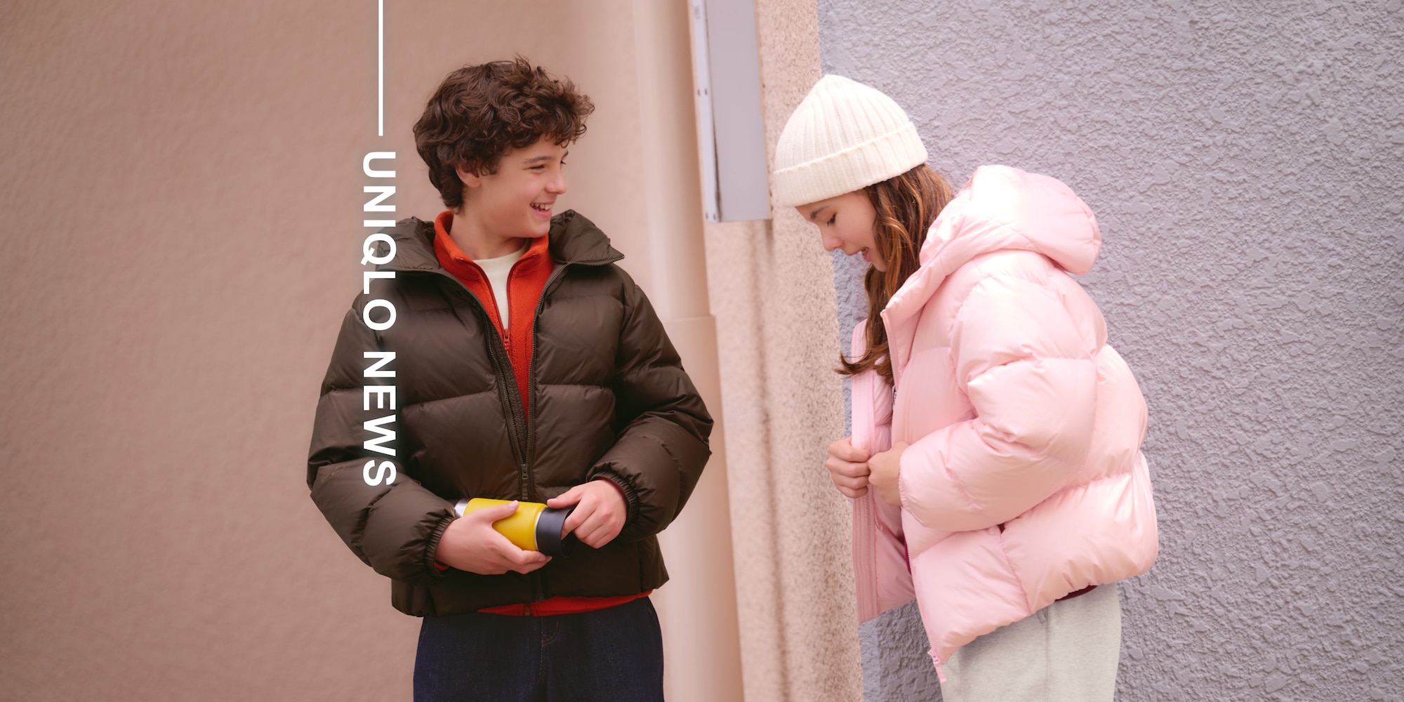 Model trägt dunkelbraune Daunenjacke, orangefarbene Fleecejacke, weißes T-Shirt und dunkelblaue Jeans.