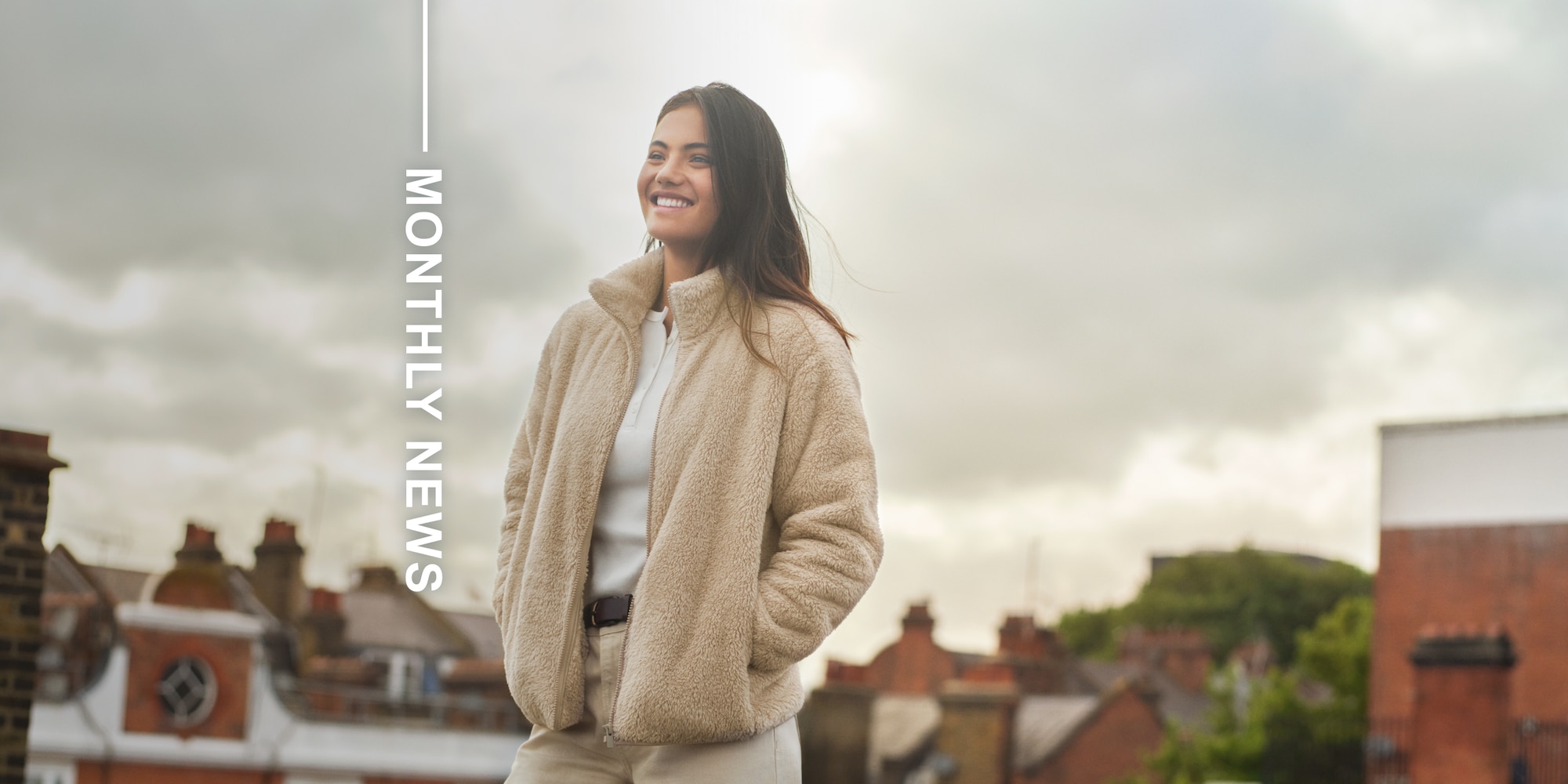 Professional Tennis Player Emma Raducanu wearing a beige fleece jacket over a white henley, beige trousers and a belt