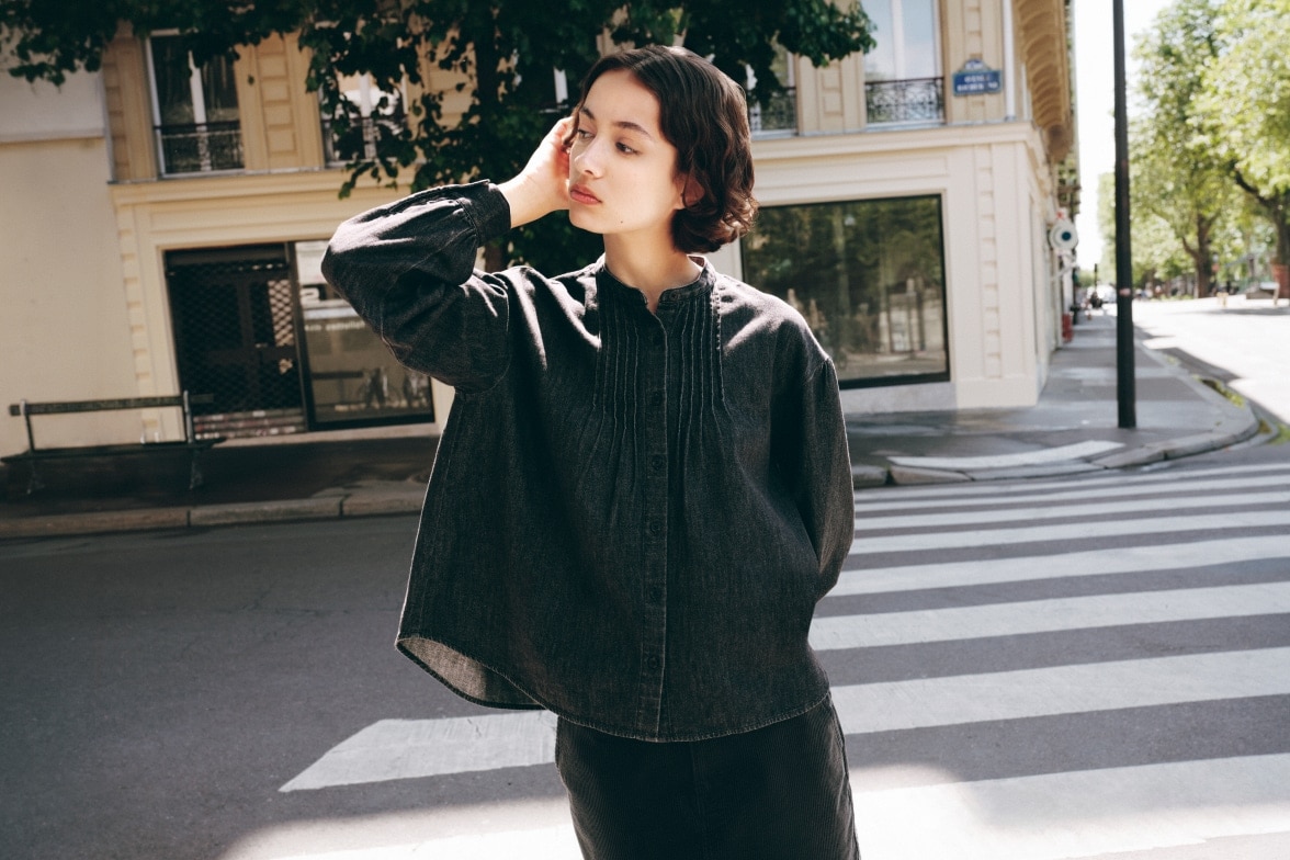 model wearing dark grey shirt with pin tucks while stood on a street in Paris