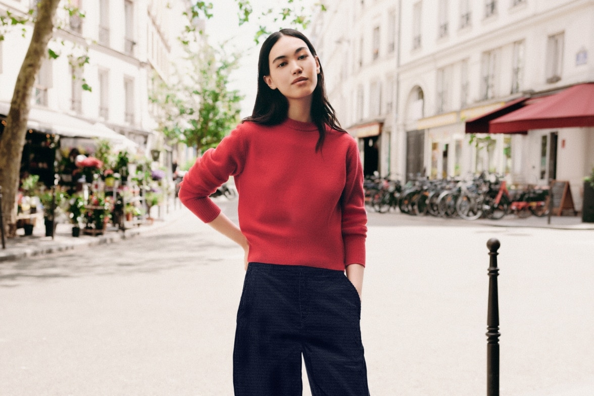 model wearing red jumper and black trousers while stood on a Parisian street