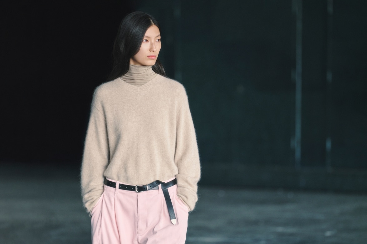 model wearing oatmeal V neck knit over an oatmeal turtleneck thermal top with pink trousers and a black belt