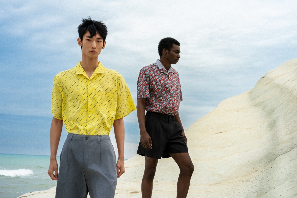 two models wearing patterned short sleeved shirts in yellow and red with grey trousers and black shorts