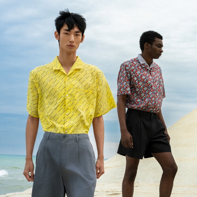 two models wearing patterned short sleeved shirts in yellow and red with grey trousers and black shorts