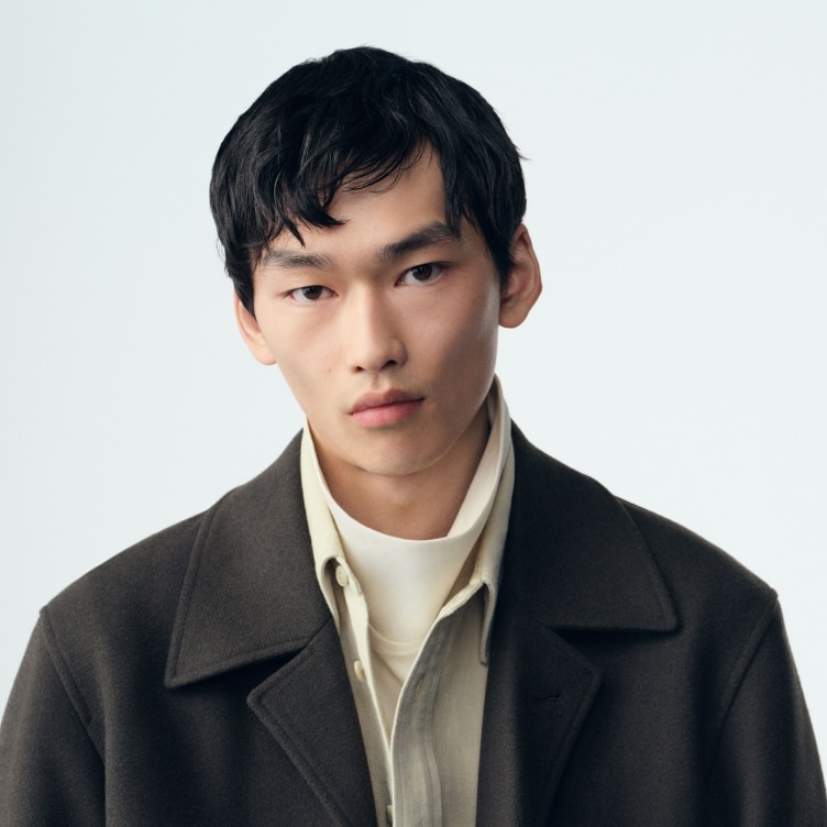 model wearing dark grey overcoat over an off white shirt and white turtleneck