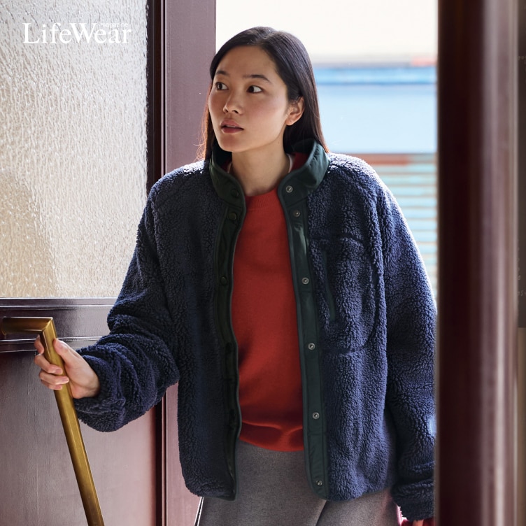 model wearing Pile Lined Fleece Combination Jacket, 100% Cashmere Crew Neck Jumper, Brushed Jersey Flared Skirt and Soufflé Yarn Triangle Scarf while opening the door to a café