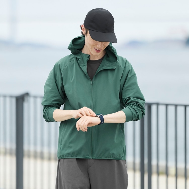 model wearing 2-Way Stretch Cap in black, green jacket and grey joggers while outside by the water
