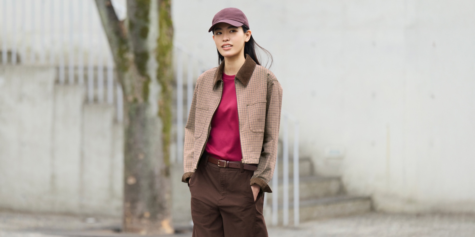 Model wearing a Uniqlo Zip-Up Short Jacket (Patterned), burgundy T-shirt, brown trousers, and a cap, standing outdoors in an urban setting.