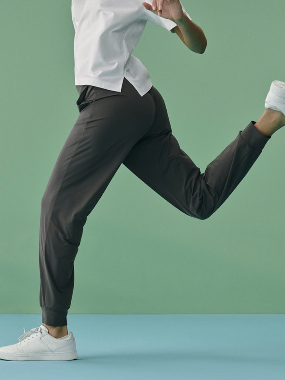 model wearing Ultra Stretch Joggers in dark grey with a white T-shirt and trainers, mid-run