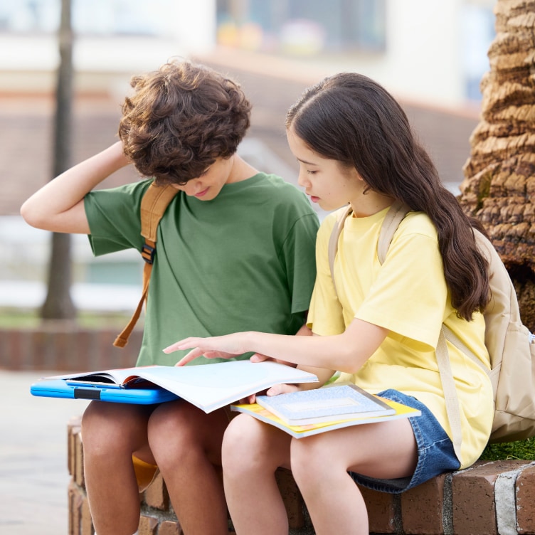 two models wearing AIRism Cotton Crew Neck T-Shirts while sat outside on a wall looking at a book together
