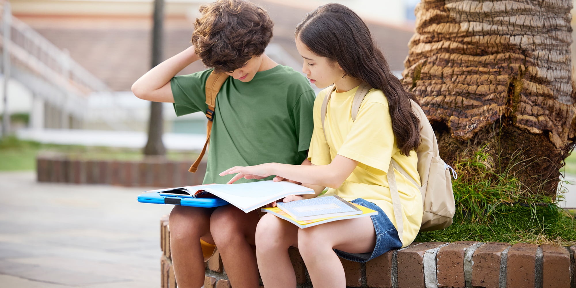 two models wearing AIRism Cotton Crew Neck T-Shirts while sat outside on a wall looking at a book together