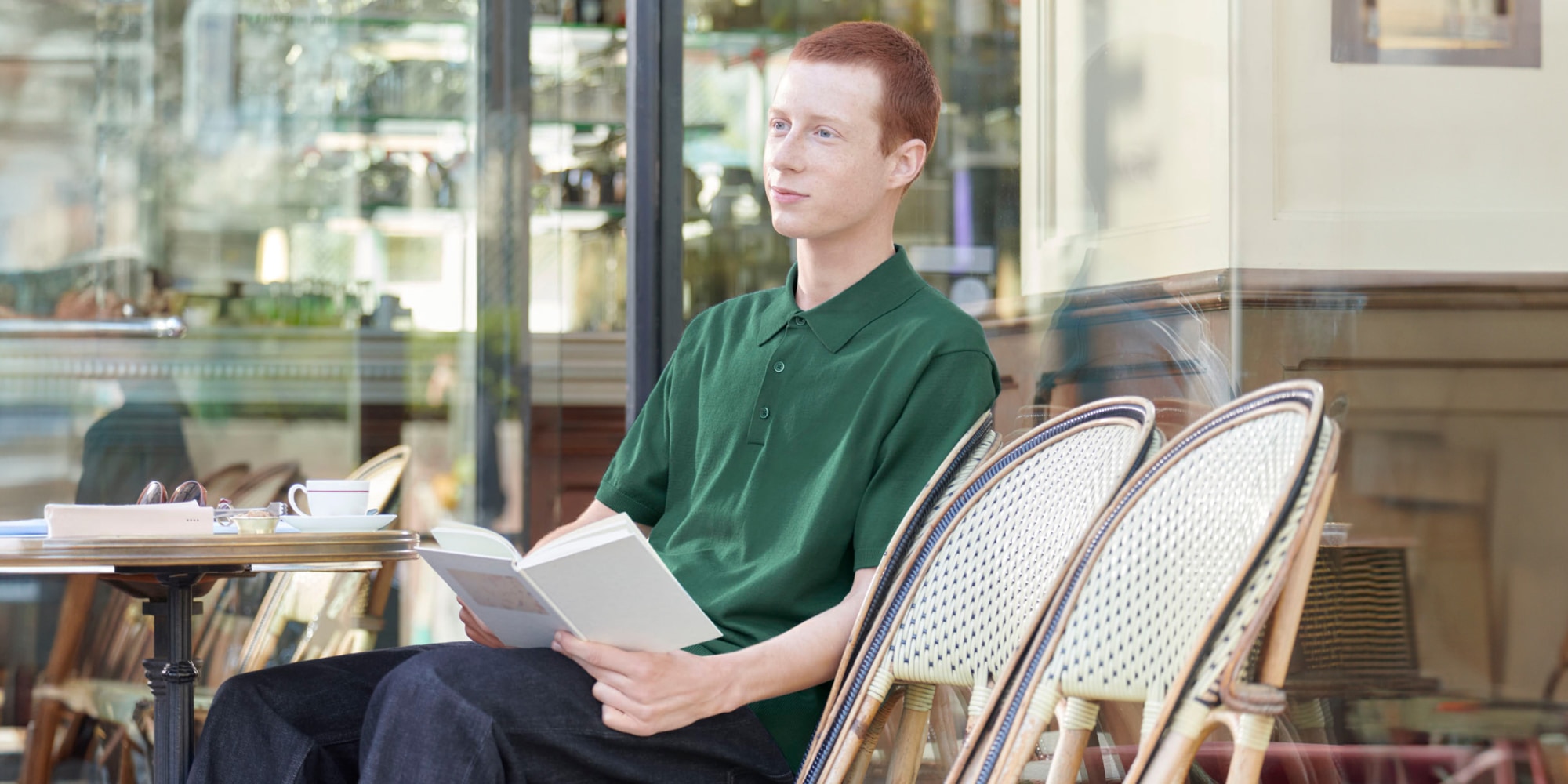 model wearing Washable Knit Polo Jumper in green with dark wash jeans while sat outside a café reading a book