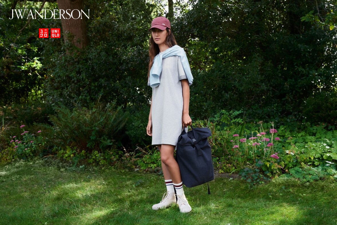 model wearing Oversized T-Shirt Dress in grey with a light blue top tied around the shoulders, a dark pink cap, white socks and off white trainers while stood in a garden