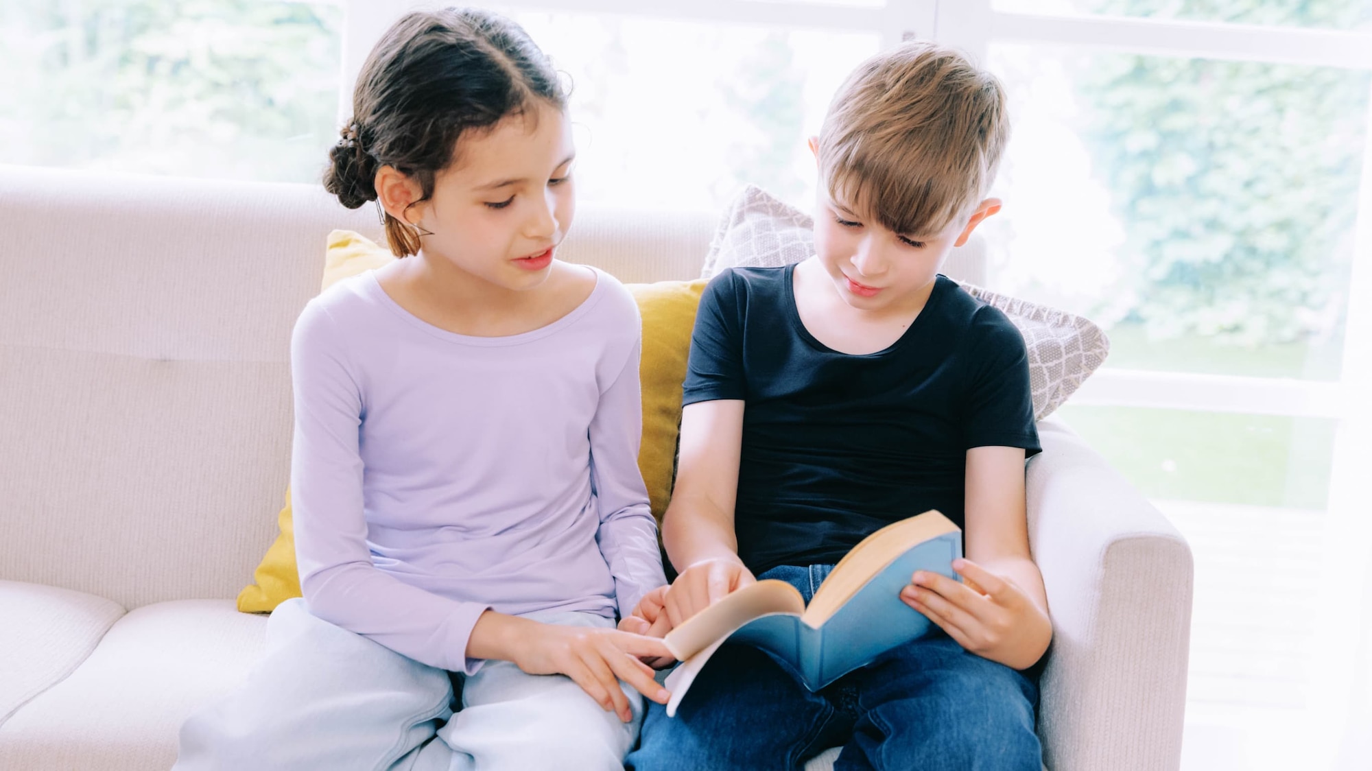two models wearing HEATTECH tops while sat on a sofa reading a book together