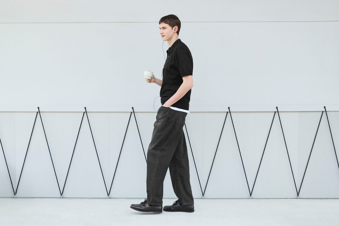 model wearing baggy jeans in dark grey with a black polo shirt layered over a white T-shirt and black shoes