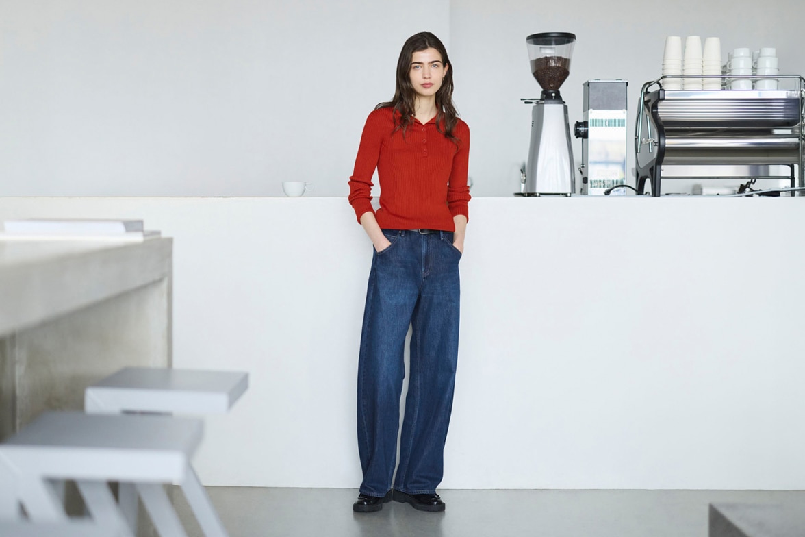 model wearing baggy barrel leg jeans in mid wash denim with a red knitted polo and black shoes while standing in a coffee shop