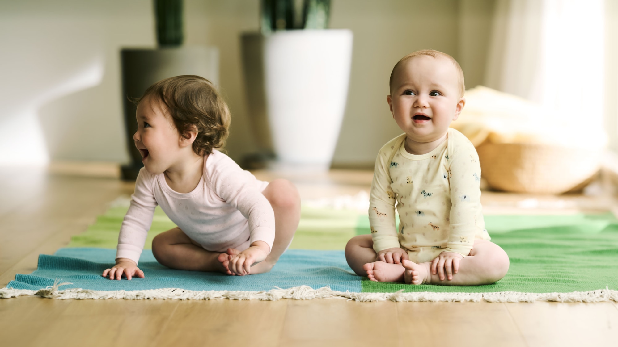 two models wearing UNIQLO bodysuits while sitting on a blanket on the floor