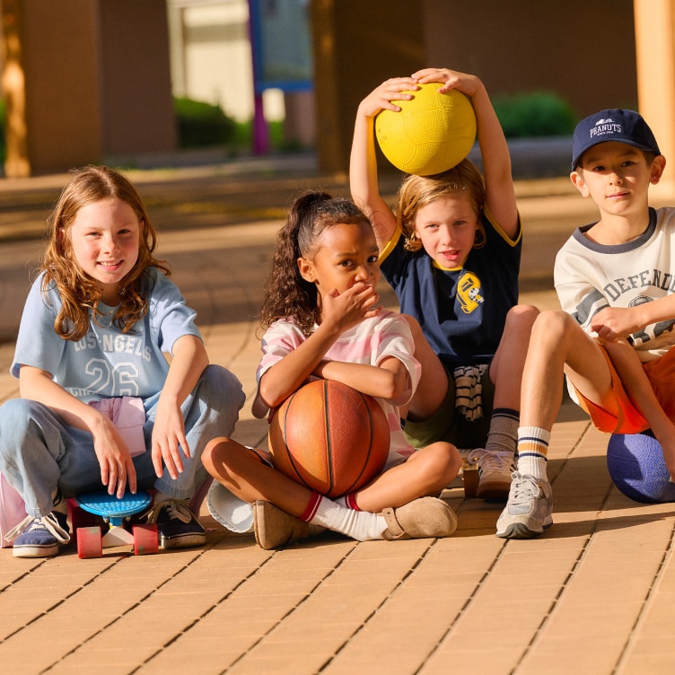 four models wearing uniqlo T-shirts while sat on the ground holding basketballs and skateboards
