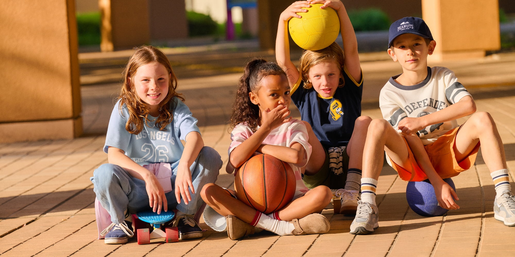 four models wearing uniqlo T-shirts while sat on the ground holding basketballs and skateboards