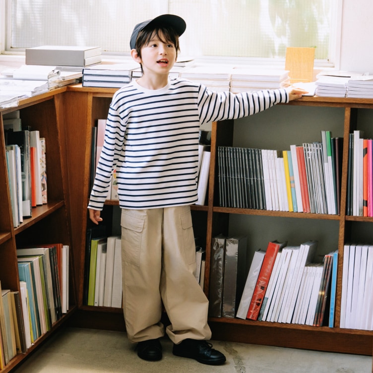 model wearing AIRism Cotton Crew Neck T-Shirt in navy with beige cargo trousers and a cap while stood next to some book shelves