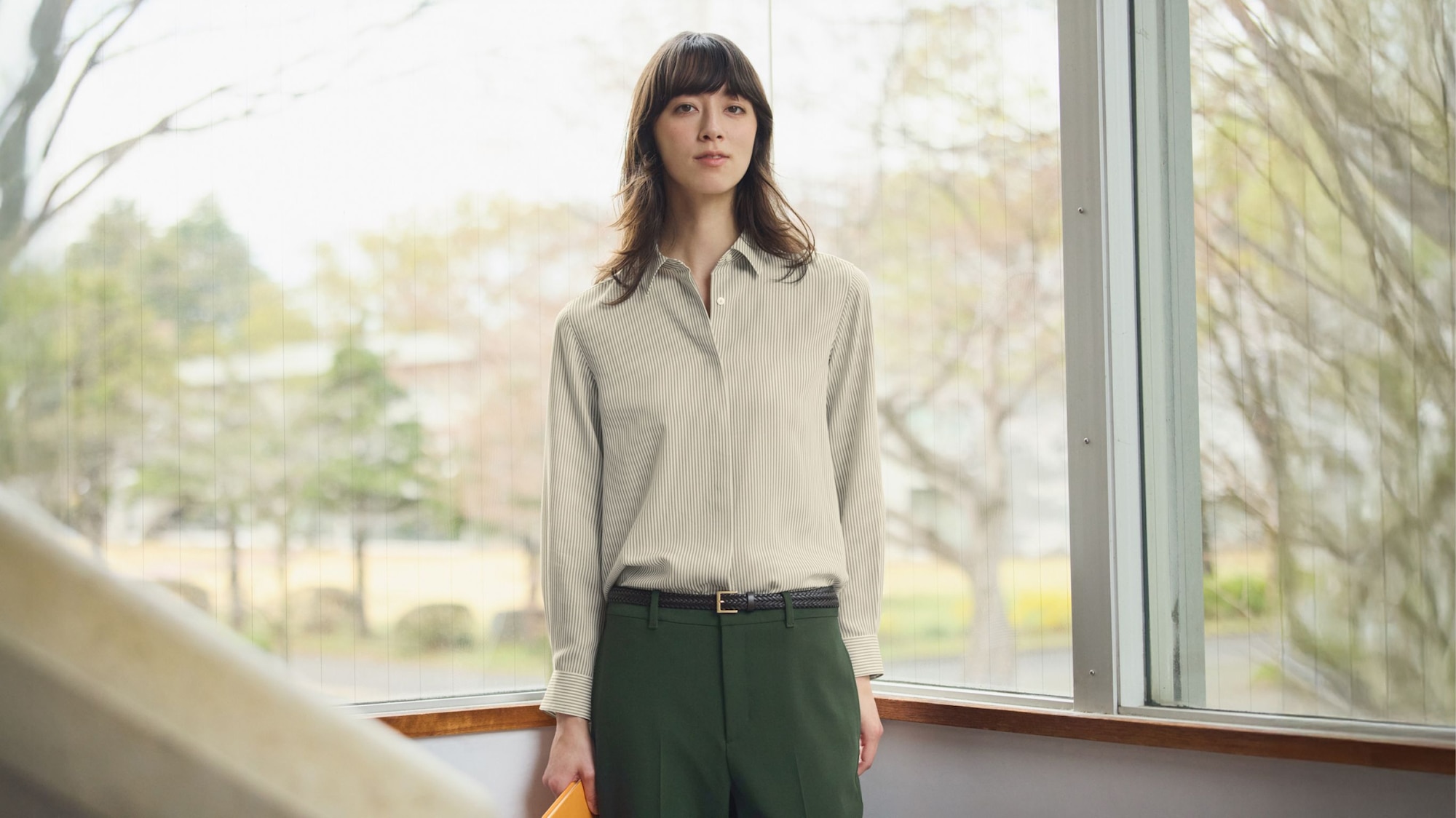 mannequin portant une chemise rayée grise et blanche à boutons dissimulés avec un pantalon vert et une fine ceinture tressée noire à boucle dorée