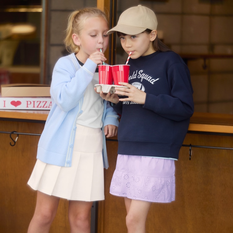 Deux mannequins portant des jupes-shorts UNIQLO boivent à la paille dans des gobelets rouges.