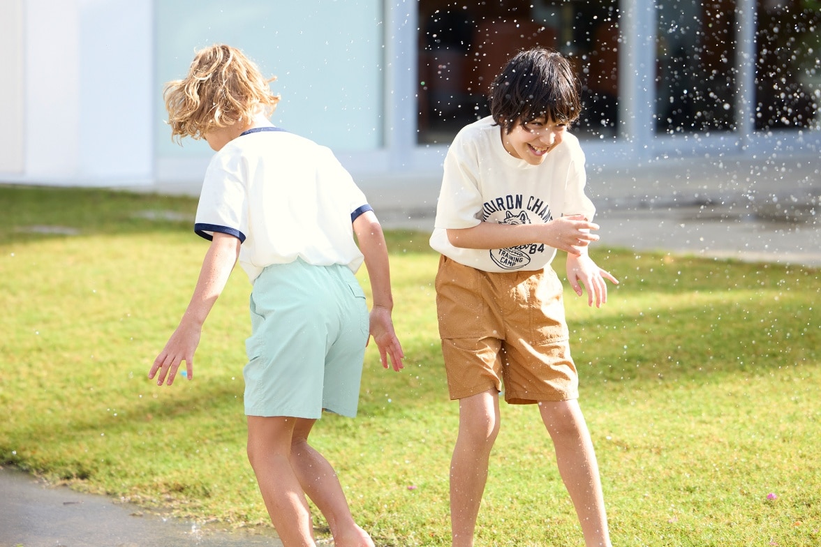 two models wearing Geared Shorts while playing outside in a garden and being sprayed with water
