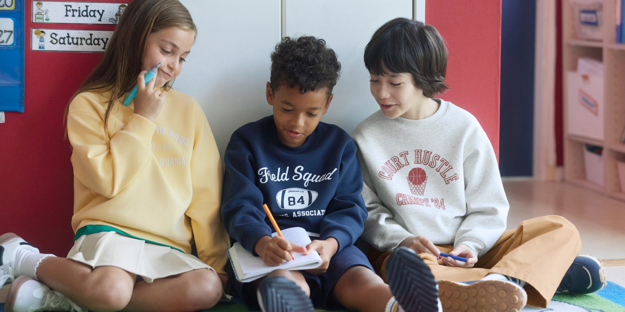 three models wearing UNIQLO sweats while sat on the floor writing in a notebook