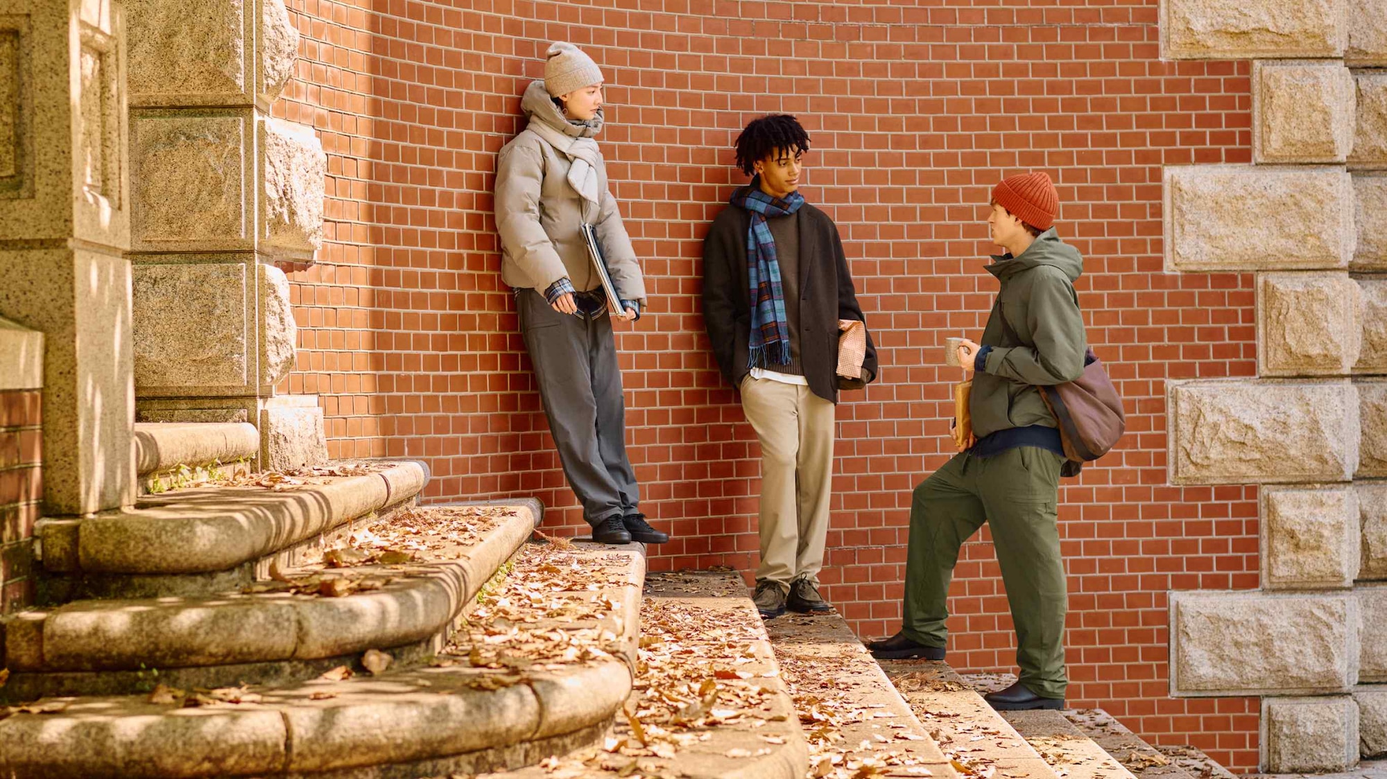 three models wearing UNIQLO warm trousers, surrounded by fallen leaves
