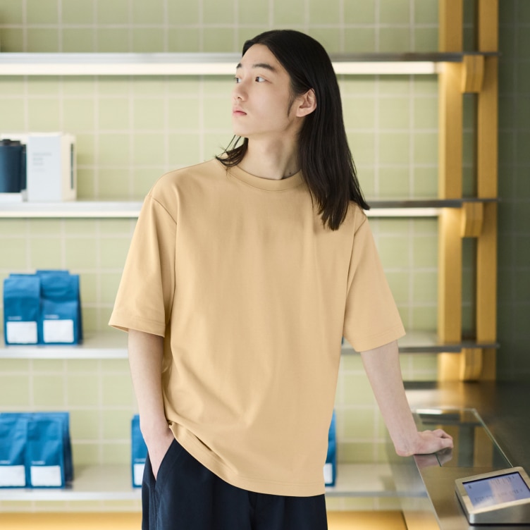 model wearing AIRism Cotton oversized crew neck T-shirt in light orange with black trousers while stood in a coffee shop