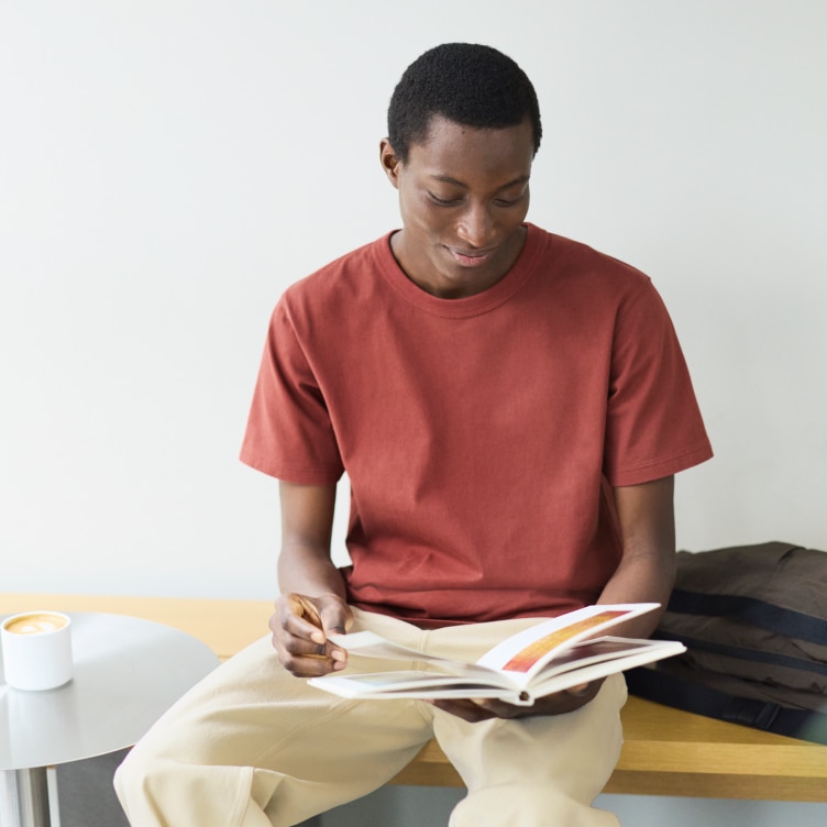 model wearing crew beck T-shirt in burnt orange with cream trousers while sitting and reading a book