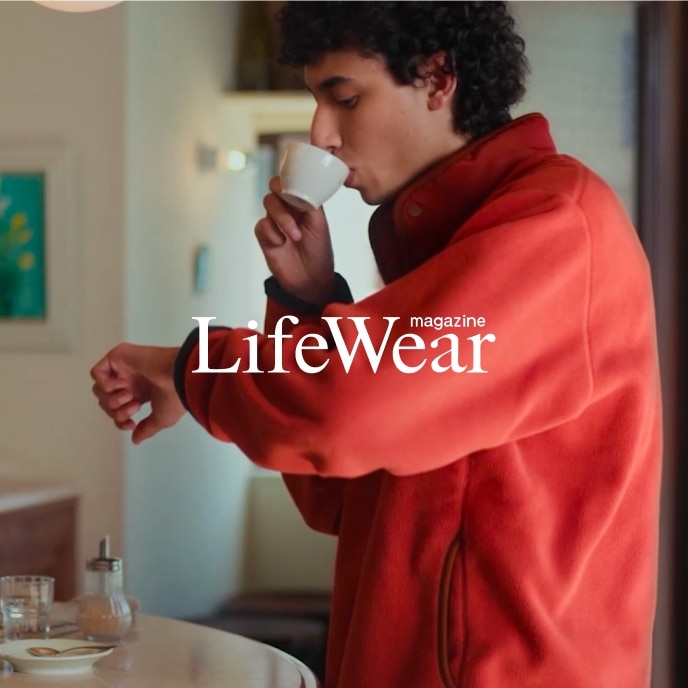 model wearing orange fleece while drinking an espresso at the counter of a café
