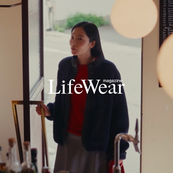 model wearing Pile Lined Fleece Combination Jacket, 100% Cashmere Crew Neck Jumper, Brushed Jersey Flared Skirt and Soufflé Yarn Triangle Scarf while opening the door to a café