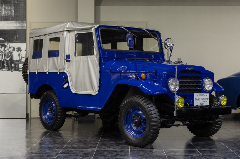 ランドクルーザー（20系）1957年 6 気筒 3878cc 105 馬力エンジン 四輪駆動 警察予備隊（現陸上自衛隊）の要請による不整地走行用クロスカントリー仕様車の入札用として開発された初代（BJ 型）のあと、民間向けの外観を備えた 2 代目の通称「20系」。強力な機動力から、陸の巡洋艦をイメージし、水中渡河、山登りでも条件問わず走破を可能にする、どんな用途にも使える万能車として進化した四輪駆動車のパイオニア。シンクロメッシュ機構、ステアリングダンパー、乗用車並のサスペンションを用いているため運転しやすく、快適な乗り心地を実現。貨客兼用からトラック、ライトバン、消防車、診療車など幅広い用途に応用された。海外への本格的な輸出をスタートしたモデルでもある。