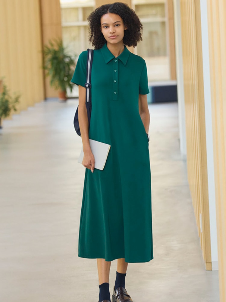 model wearing teal polo shirt midi dress with black socks and brown patent loafers, while carrying a bag and some paper