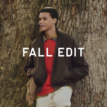 Man standing against a tree wearing brown jacket and red sweater.