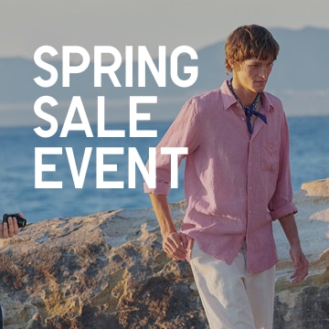 Model outside near the coast wearing a pink stand collar button up shirt and white pants.