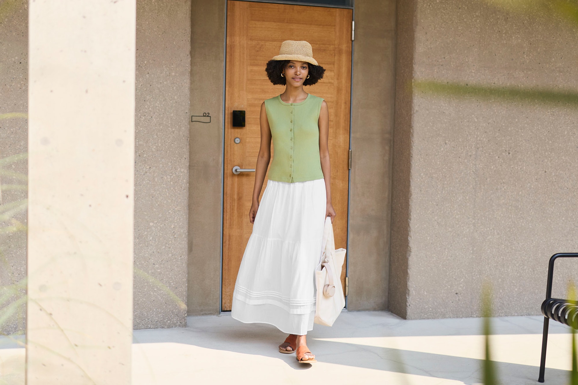 Woman outside wearing a braided brown hat, green button up sleeveless shell top, and white tiered skirt.